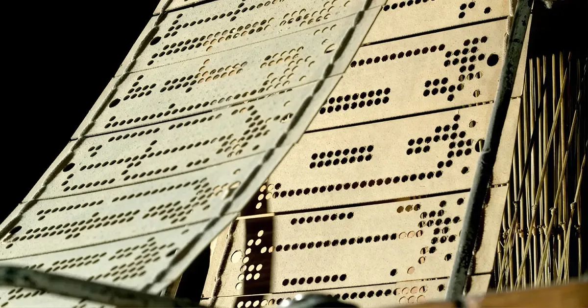Close-up of Jacquard loom punch cards laced together in a long chain, their holes forming a pattern.