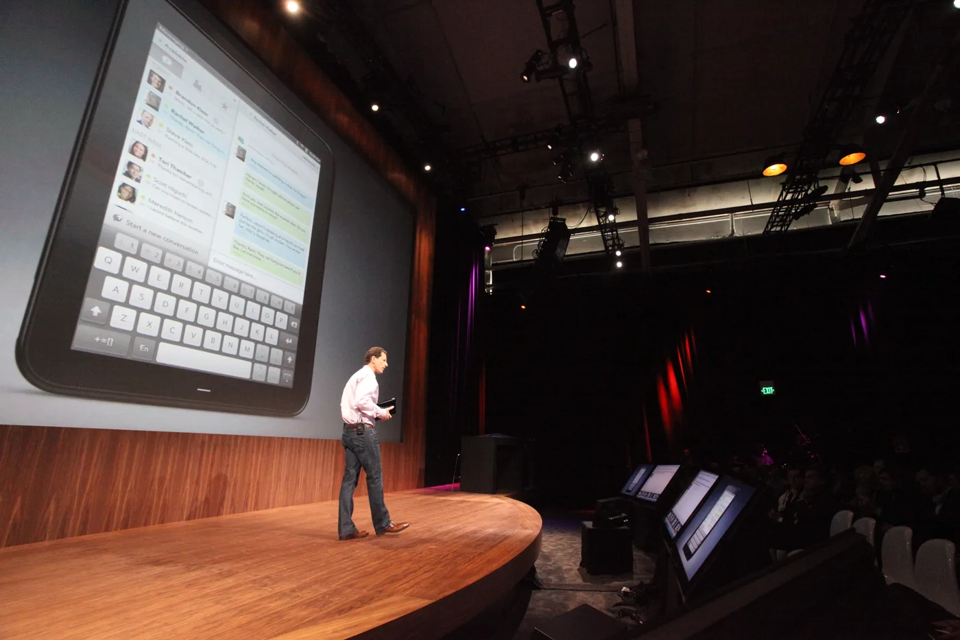 Jon Rubinstein on a dark stage, in front of a huge screen showing the HP TouchPad with its email app and on-screen keyboard.