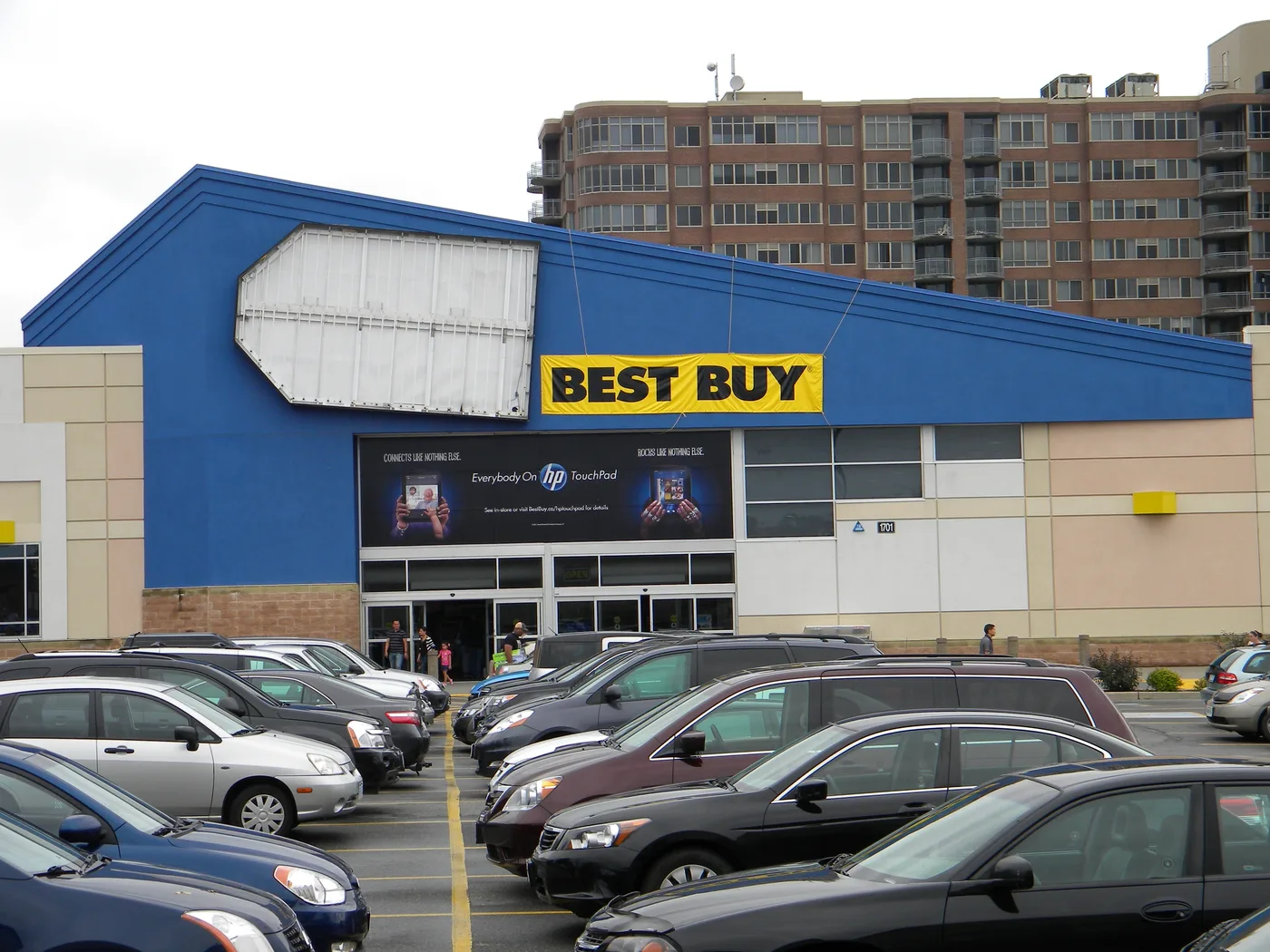 The front of a Best Buy store and its parking lot, with large banners for the HP TouchPad above the entrance.