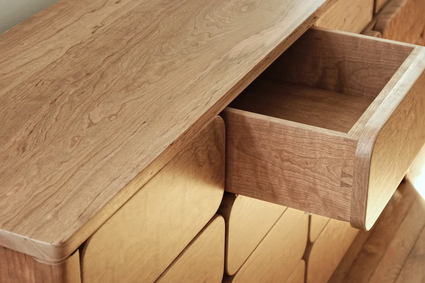 Close-up of a cherry sideboard with one dovetailed drawer pulled open.