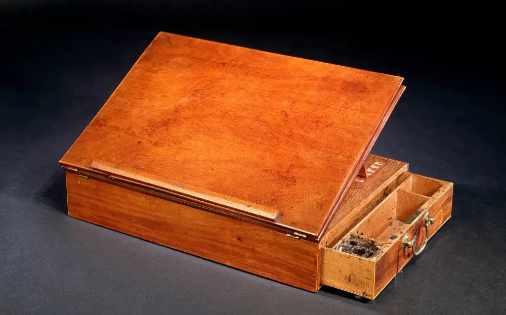 Thomas Jefferson’s mahogany writing desk, its writing board raised and its drawer open to show compartments for paper and an inkwell.